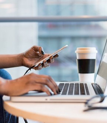 Image of a woman's hands typing on a laptop and phone